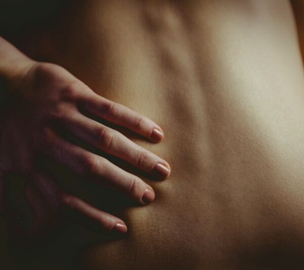 nude-woman-with-a-back-injury-on-black-background