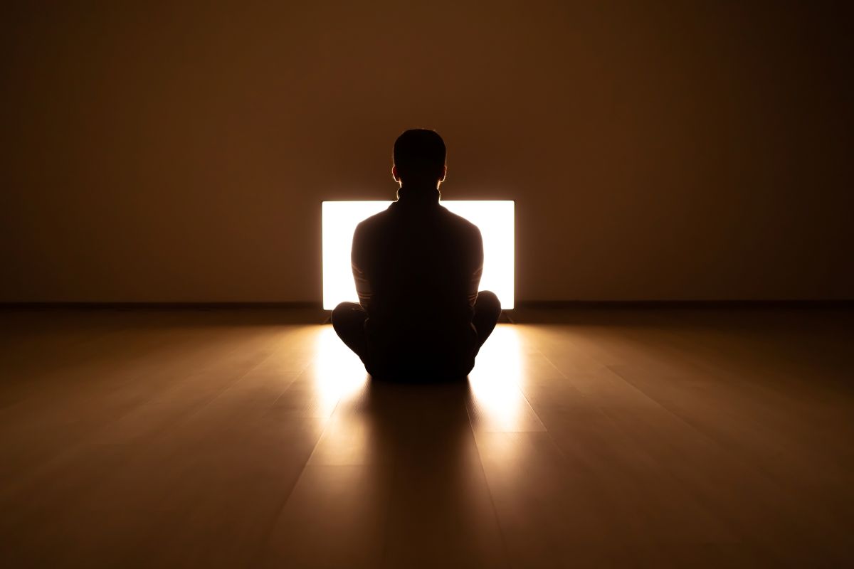Person sitting in meditative pose with warm light, reflecting calm and safety during somatic trauma therapy.